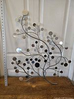 Front view of metal tree wall decor showing curved branches with circular mirrored discs, placed against a door with a ruler showing size.