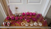 Full assortment of pink Christmas ornaments laid out on wooden surface with ruler for scale, featuring spiral tree topper, star ornaments, reindeer, spherical ornaments, heart shapes, and disco ball style ornaments.