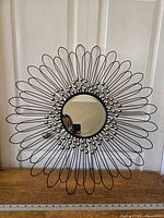 Frontal photo showing the entire metal floral mirror with reflective glass center and decorative metal flower petal frame with gold spherical accents.