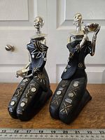 Front view of two kneeling African figurines side by side showing detailed decorations and measurements.