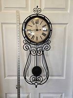 Front view of Sterling & Noble pendulum wall clock hanging on white door with a measurement ruler beside it showing approx. 32 inches in height and 12 inches in width.