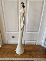 Full view of tall ceramic geisha figurine standing against white door background, showing height and detail.