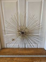 Front view of vintage gold starburst wall art showing radiating metal rods and woven circular center against a white door background. Includes measuring tape showing 28-inch diameter.