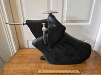 Front profile photo of large black samurai statue holding an extended katana sword, placed on wooden surface with a ruler for scale.