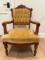 Front view of antique armchair showing carved wooden frame, tufted gold velvet upholstery on backrest, and seat cushion.