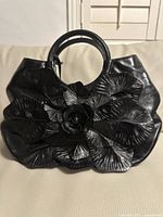 Front view of black leather handbag with large flower appliqué