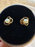 Pair of pearl stud earrings with gold love knot setting displayed on black velvet.