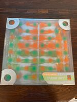 Original box packaging of the neon orange and green chess set showing the pieces arranged inside clear plastic molding and visible signs of wear on box edges.