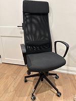 Front view of black mesh office chair featuring high back with headrest, padded fabric seat, armrests, and wheeled base.