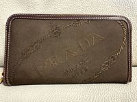 Front view of the Prada brown canvas and leather zippered clutch wallet with logo visible