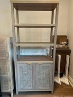 Front view showing three open shelves above and two fabric front doors below with gold handles.