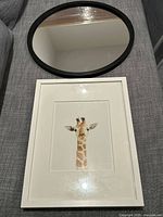 Both the round black rubberized mirror and the giraffe print framed wall art laid on a couch surface.