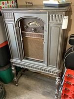 Front view showing wooden cabinet with carved details, sliding doors, radio dial, and speaker grille.