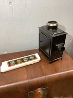 Front angle view of the black metal kerosene lantern style slide viewer next to a protective sleeve containing painted glass slides.