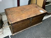 Perspective front and side view of aged wooden chest with rope handle and scuffed sides.