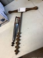 Top-down view of the two antique auger tools placed on a white table surface showing the full length and wooden handles.