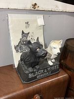 Carved wood Black & White Scotch Whisky advertising display with two dogs and paper advertisement behind.