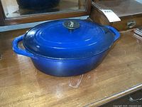 Blue enamel-coated cast iron roaster with lid on wooden surface showing minor wear.