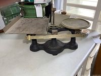 Side view of antique Fairbanks cast iron balance scale with brass trays and measuring rod on a white table.
