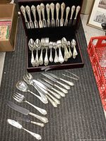 Full view of the Alpacca flatware pieces arranged inside and outside the wooden chest, showing spoons, forks, knives, and serving utensils.