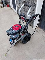 Full front view of the pressure washer on concrete, showing frame, wheels, red engine cover, hose and wand attached.