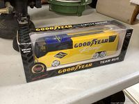 Front side view of the Goodyear Racing Team Bus diecast model in its original sealed box showing yellow and blue colors and Goodyear logos.