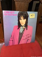 Front cover of Joan Jett & the Blackhearts I Love Rock 'n Roll LP record showing Joan Jett in a pink jacket with a blue scarf against a purple-blue background. The cover shows minor wear.