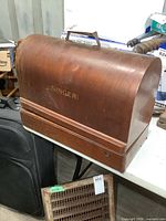 Curved wooden case with handle, Singer logo on side, showing wood wear and patina