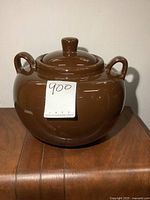 Front view of the large brown stoneware bean pot with two handles and lid, placed on a wooden surface.