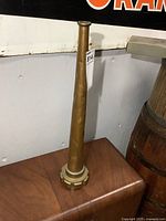 Full view of the vintage fire hose nozzle standing upright showing tapered copper body and brass base.