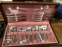 Open pink velvet-lined chest showing full set of silver Community South Seas flatware including various forks, spoons, knives, and serving pieces arranged in slots and straps.