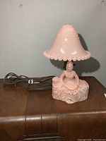 Front view of the vintage pink glass lamp with figurine base and glass shade on a wooden surface.