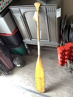 Full view of the wooden Lolk paddle standing upright beside furniture to show length and overall condition.