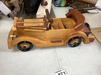Side and front angled view of handmade wooden vintage car showing detailed wooden wheels, seats and convertible roof.