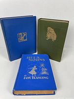 Three hardcover vintage books: a blue book The Midnight Folk, an olive-green Mr. Punch's History of The Great War, and a bright blue Hula Moons showing wear at spine base.