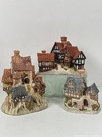 Three collectible cottages by David Winter arranged with varied angled views showing details of roofing, chimneys, and stonework.