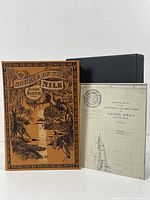 Front cover showing detailed pictorial cloth design with title and author, book standing next to slipcase and folded map inserted.