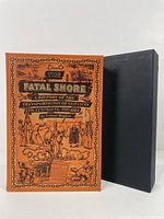 Front cover of the hardcover book 'The Fatal Shore' by Robert Hughes, showing orange cover with black detailed illustrations and matching black slipcase beside it.