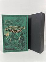 Front view of green hardcover book 'History of The Conquest of Mexico' by William Prescott, showing detailed embossing and illustrations with slipcase beside it.