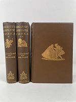 Three volumes showing front covers with gilt embossed artwork depicting period figures; each book is bound in brown cloth.