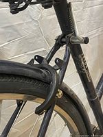Photo showing rear wheel with attached Dutch style lock mounted above tire secured to frame, part of back mudguard visible.