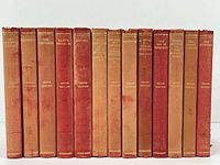 Front view of 13 red leather bound volumes by John Galsworthy, titles clearly visible on spines with gilt lettering. Show wear and color fading.