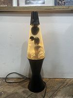 Front view of a 16 inch tall lava lamp with black base and top. Inside clear liquid are black wax blobs decorated with white skull and crossbones motifs, illuminated and floating.