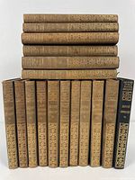 17 volumes of leatherette bound Charles Dickens works, spines facing forward stacked in two rows showing gilt detailing.