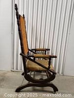 Side view of the antique rocking chair showing the wooden frame, fabric upholstery, and iron spring rocker base.