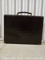 Front exterior view of dark brown crocodile skin briefcase with sturdy handle and gold-tone lock.