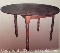 Photo of oval drop leaf wooden dining table with turned legs showing two demilune leaves fully extended, creating oval surface.