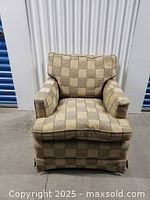 Front angle photo of mid-century upholstered armchair with checkered upholstery showing seat cushion, armrests, and partial ottoman in front