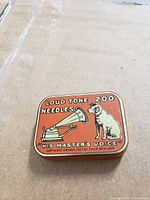 Red metal tin with gramophone and dog image reading Loud Tone 200 Needles His Master's Voice, shows wear and scratches.