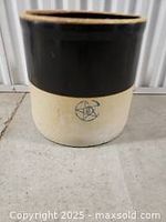 Side view of glazed clay planter showing black upper section and cream lower section with star logo.